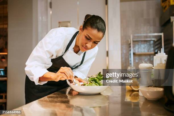 focused female chef finishing salad with cilantro using tweezers in commercial kitchen - garnish stock pictures, royalty-free photos & images