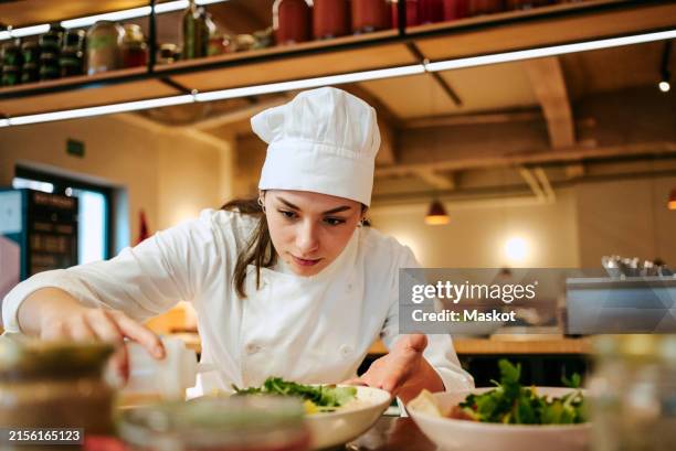 close-up of female chef pouring dressing oil on salad at commercial kitchen - koksmuts stockfoto's en -beelden