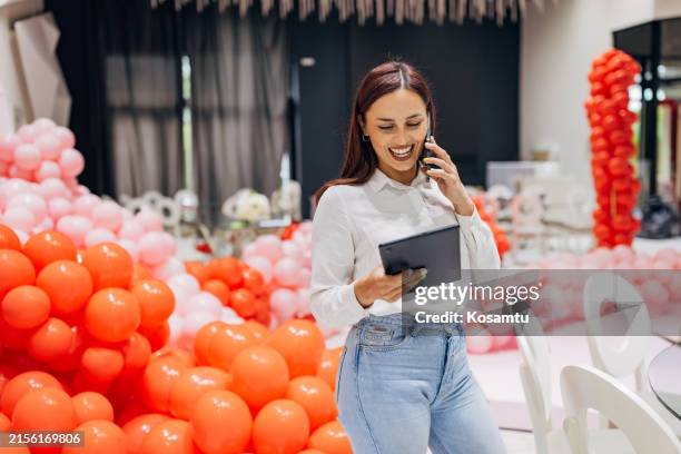 una organizadora de eventos habla por teléfono móvil con nuevos clientes mientras supervisa la decoración del salón de fiestas - organizador de eventos fotografías e imágenes de stock