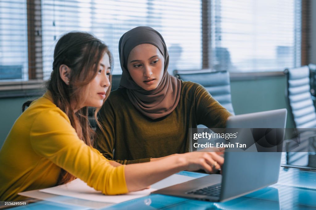 Two Asian businesswomen talking while working together with laptop in a modern office startup