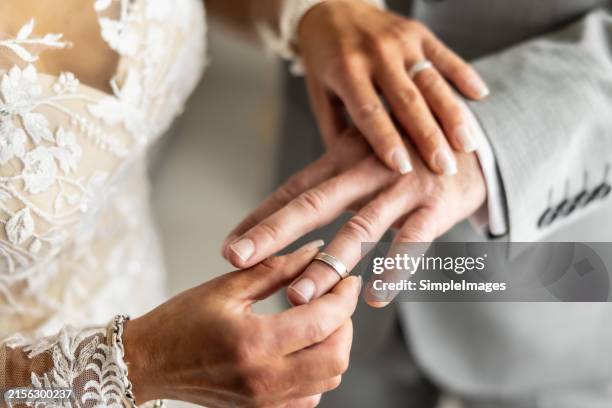 wedding rings exchange with bride putting a ring on her future husband's finger. - promesas de matrimonio fotografías e imágenes de stock