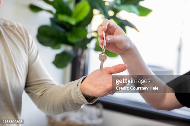 an open hand reaches for a silver key on a white key ring while another person hands it to them. - notary stock pictures, royalty-free photos & images