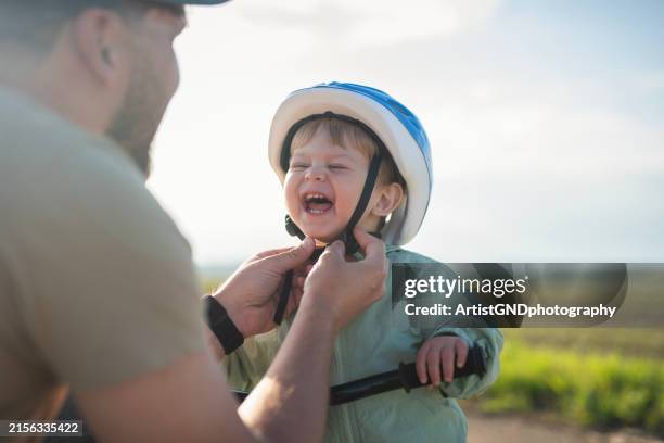 father preparing his little boy for a bicycle ride. - cycling helmet stock pictures, royalty-free photos & images
