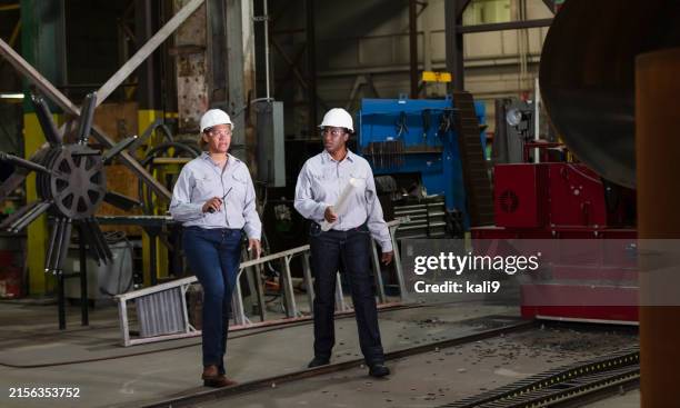 two multiracial women engineers walking in warehouse - steel worker stock pictures, royalty-free photos & images