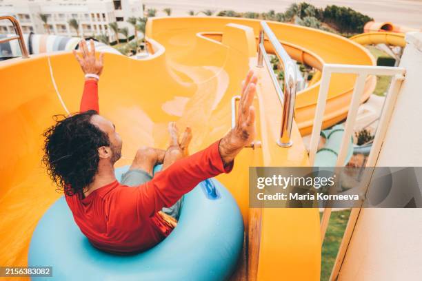 man having fun while sliding into the swimming pool. - adrenalina fotografías e imágenes de stock