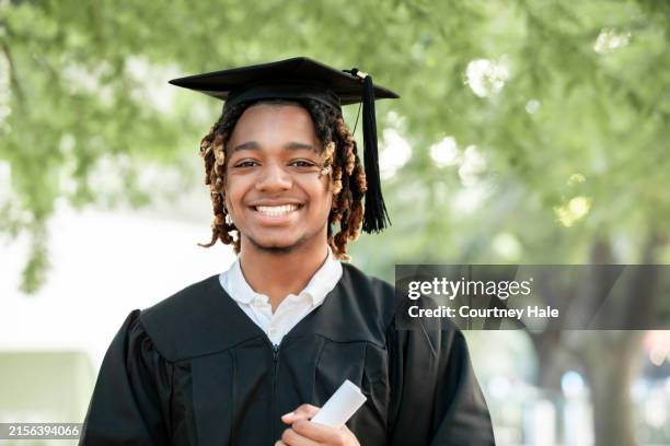 un encantador joven negro sonríe a la cámara en su graduación. - toga fotografías e imágenes de stock