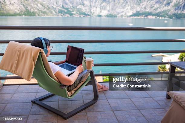 mid-adult caucasian woman having an video call on laptop from the balcony with an view of sea and mountain - flexible screen stock pictures, royalty-free photos & images