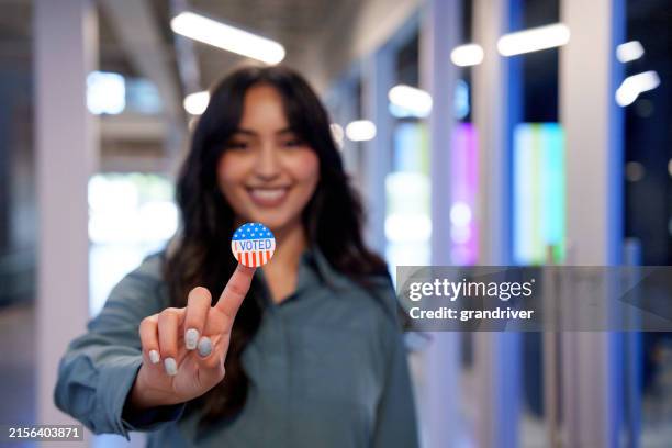 young hispanic woman in her twenties proudly displaying her i voted sticker in a co-working space - stemmen stockfoto's en -beelden