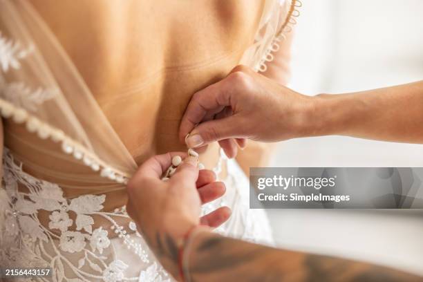 the bridesmaids help the beautiful bride get ready for the wedding. beautiful woman hands dressing and buttoning dress. - trouwjurk stockfoto's en -beelden