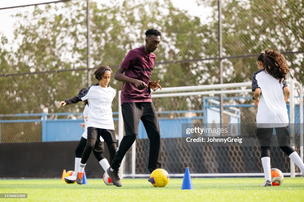 Coach with soccer ball practicing amidst female soccer team