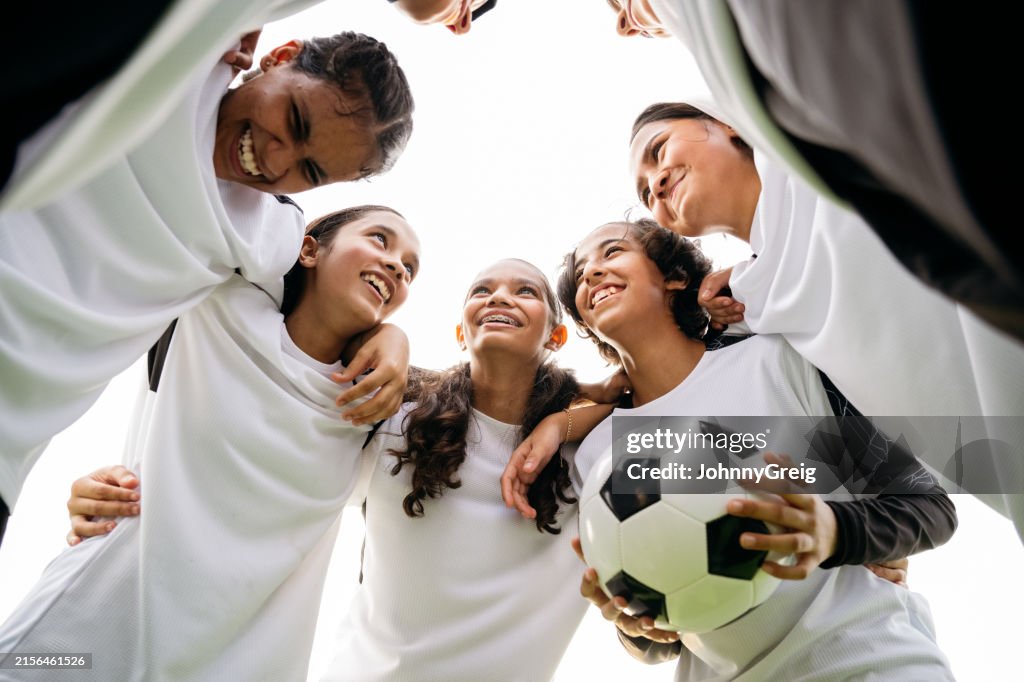Female soccer players standing in huddle with ball