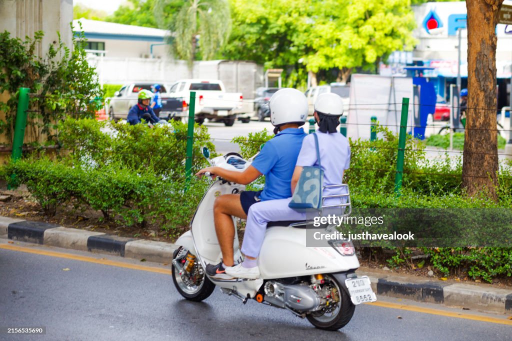 Seitliche Rückansicht eines thailändischen Paares, das in Bangkok auf Vespa fährt