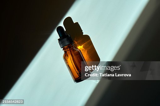 Amber Glass Dropper Bottle in Sunlight with Hard Shadows. Top View, Flat lay, with Copy Space. Seasonal skincare, innovational health care technologies concept Amber Glass Dropper Bottle in Sunlight with Hard Shadows. Top View, Flat lay, with Copy Space. Seasonal skincare, innovational health care technologies concept