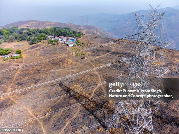 hard to reach small village over a hill top with and electrical grid power lines transmitting power - energieerzeugung stock-fotos und bilder