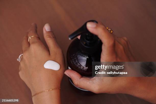 an asian woman applies body lotion on skin - creme corporal imagens e fotografias de stock