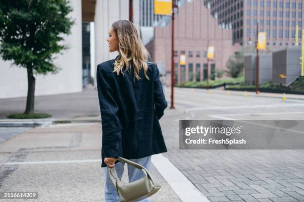 selbstbewusste frau, die mit handtasche in der städtischen straße geht - handtasche stock-fotos und bilder