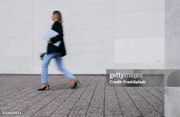 businesswoman walking outdoors holding a laptop and documents - high heels walking stock pictures, royalty-free photos & images