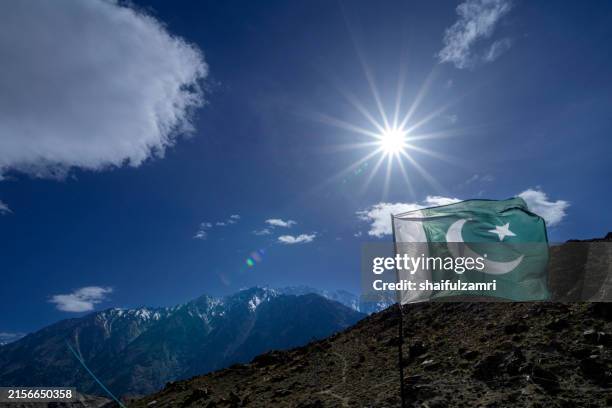 the flag of pakistan waves freely in the summer breeze against the majestic backdrop of the karakoram mountain range. - india pakistan stock pictures, royalty-free photos & images