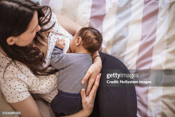 mother breastfeeding baby in cozy bedroom - breastfeeding stock pictures, royalty-free photos & images