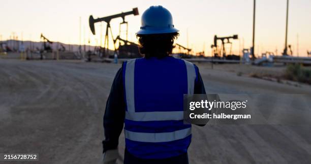 oilfield worker looking at pump jacks at sunset - oil field stock pictures, royalty-free photos & images