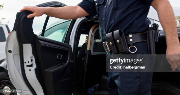 toma a nivel de la cadera del oficial de policía cerrando la puerta del coche patrulla - cuerpo de policía fotografías e imágenes de stock