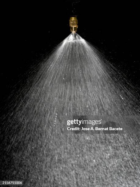 sprinkler releasing drops of pressurized water on a black background. - sprinkler stock pictures, royalty-free photos & images