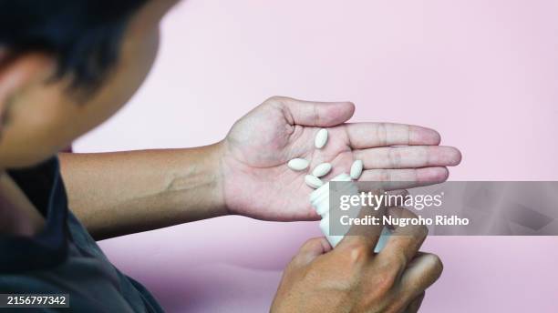 man pouring medicine pill from bottle to the hand over shoulder angle view - painkiller stock pictures, royalty-free photos & images