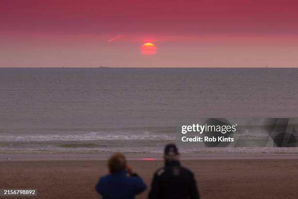 man and woman watching the sunset on texel beach - waddeneilanden stockfoto's en -beelden