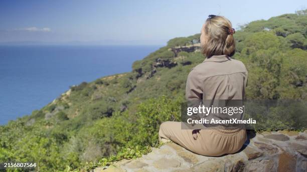 young woman sits on wall above sea - medium length hair stock pictures, royalty-free photos & images