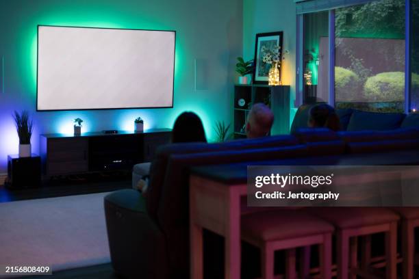 gruppo di amici che guardano la tv con luci intelligenti multicolori che illuminano il muro. un maschio, due femmine. - home cinema foto e immagini stock