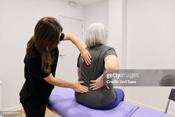 fisioterapeuta joven masajeando la espalda durante la sesión de fisioterapia en el centro de rehabilitación - osteoporosis fotografías e imágenes de stock