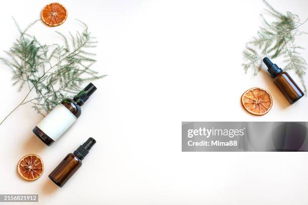 set of natural organic skincare cosmetics and essential oil in dark amber glass bottles with green twig and dried orange slices on beige background - flat lay stock pictures, royalty-free photos & images