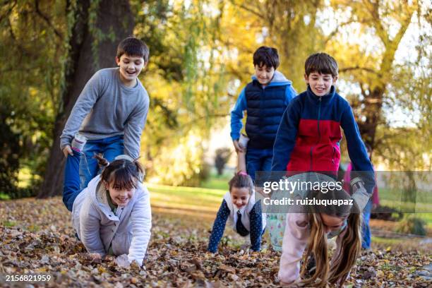 happy children playing wheelbarrow race - kruiwagen stockfoto's en -beelden