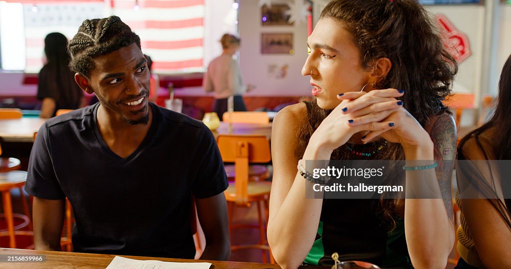 Dos jóvenes adultos sonríen durante una conversación en un bar restaurante bien iluminado - Day