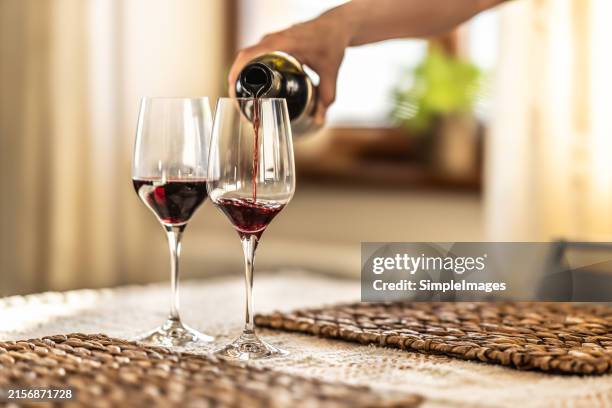 someone's hand pouring red wine into a wine glass in a home environment. - cabernet sauvignon grape stock pictures, royalty-free photos & images