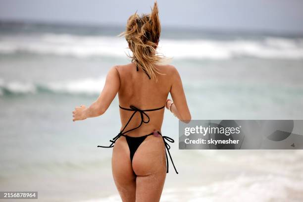rückansicht einer frau, die an einem sommertag am strand läuft. - stringtanga stock-fotos und bilder