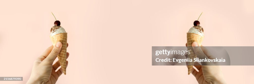 Woman's hand holding an ice cream cone on a pink background.