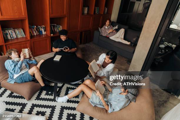 travelers relaxing with books in hostel lounge - hostel stock pictures, royalty-free photos & images