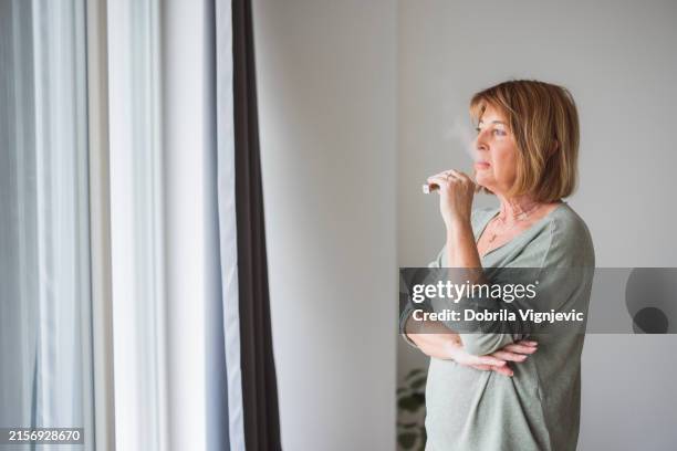 seniorin mit einer elektronischen zigarette am fenster - think tank stock-fotos und bilder