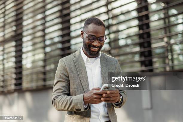 un jeune homme d’affaires utilisant un téléphone portable en marchant dans la ville - message sms photos et images de collection
