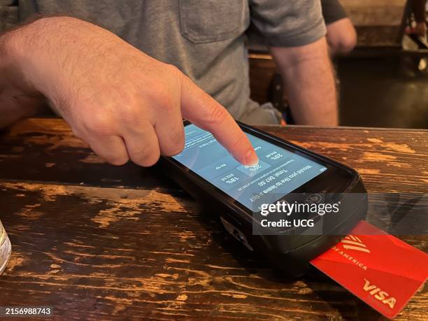 Man selecting 20% tip while using hand held credit card scanner at restaurant, Queens, New York.