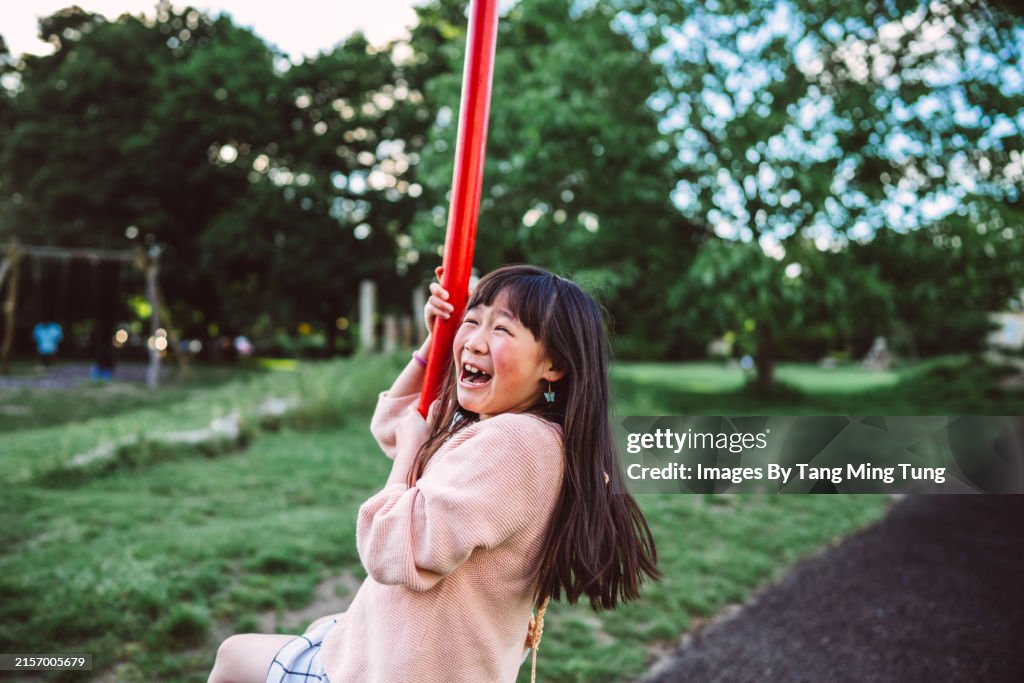 Young cheerful girl playing on a swing set at the playground