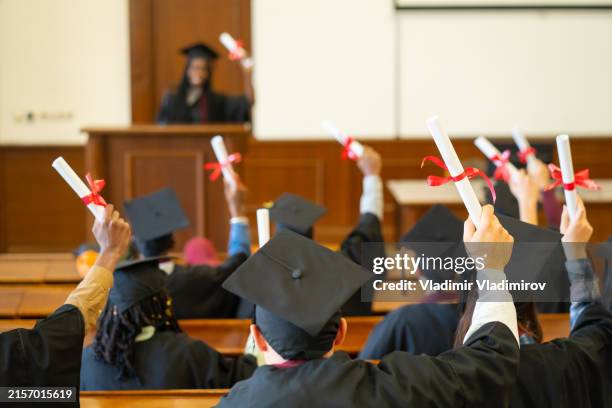 graduates waving their certificates to the valedictorian speaking from the stage - graduation valedictorian stock pictures, royalty-free photos & images