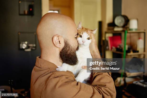 the man gently holds the domestic cat, burying his face in its soft fur. - complètement chauve photos et images de collection