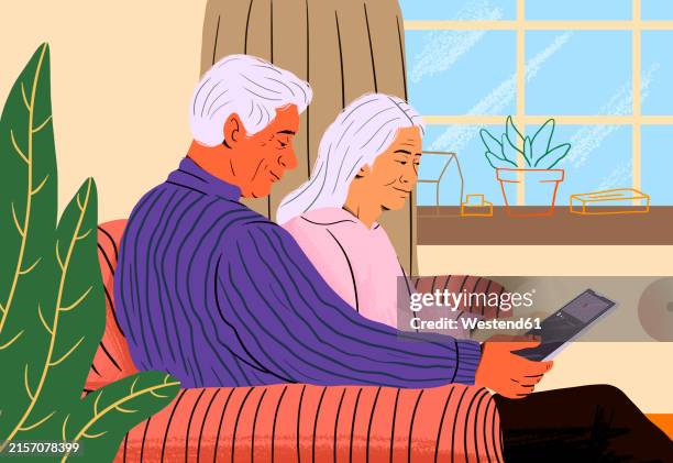 elderly couple sharing tablet and sitting on sofa at home - retirement living stock illustrations