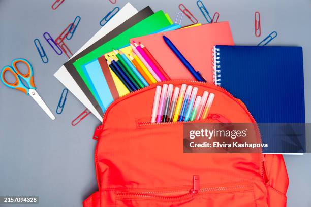 open red backpack with school supplies with colored pencils, paper clips and notebooks on a gray background. colorful school theme, copy space - material escolar fotografías e imágenes de stock