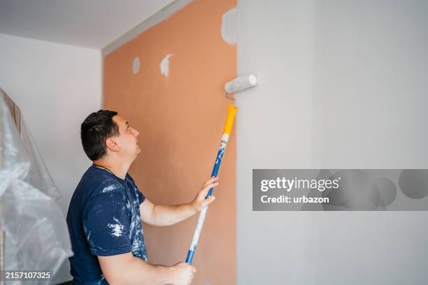 mid-adult man painting the walls in his apartment - måla bildbanksfoton och bilder