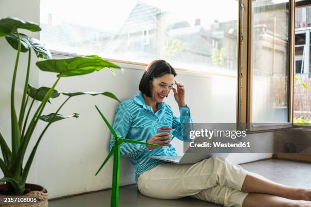 smiling businesswoman wearing smart glasses sitting with laptop and coffee cup in office - datenbrille stock-fotos und bilder