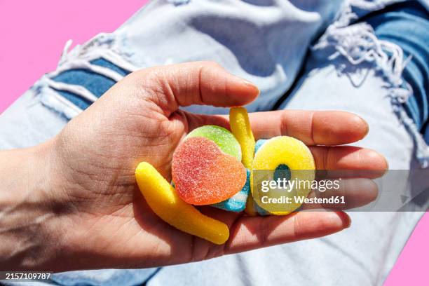 hand of woman holding jelly candies over torn jeans - gummy snoep stockfoto's en -beelden