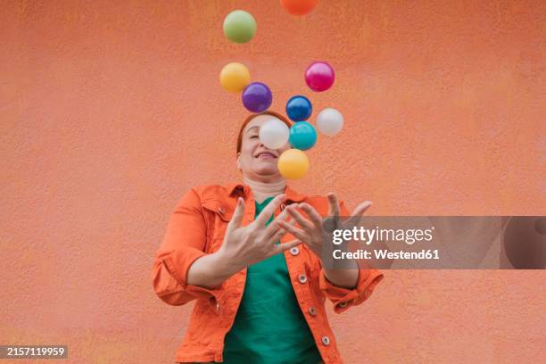 mature woman juggling multicolored balls in front of orange wall - juggling stock pictures, royalty-free photos & images